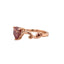 A rose gold ring with a pink heart shaped diamond center stone. Featuring curved design with two garnet accent stones. 