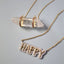 Product picture of a bubble font gold name necklace with a diamond pave frame. This necklace is a statement necklace that reads "Happy". Showing with our crystal power necklace.