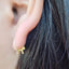 Picture of gold cat earring on the ear. The cat's tail is curved up and can be thread through the piercing and the body of the cat rests against the ear lobe creating a subtle yet sparkly affect. 