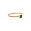 Product picture of a dainty gold band with a princess cut emerald bezel set with two small stones on on side of the band. 